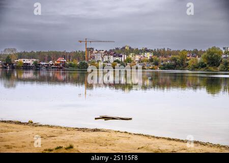 Vista panoramica degli edifici residenziali danneggiati a Irpin, Ucraina, vicino a un tranquillo lago tra gli alberi autunnali Foto Stock