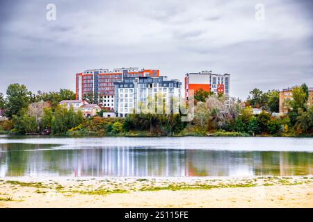 Vista panoramica degli edifici residenziali danneggiati a Irpin, Ucraina, vicino a un tranquillo lago tra gli alberi autunnali Foto Stock