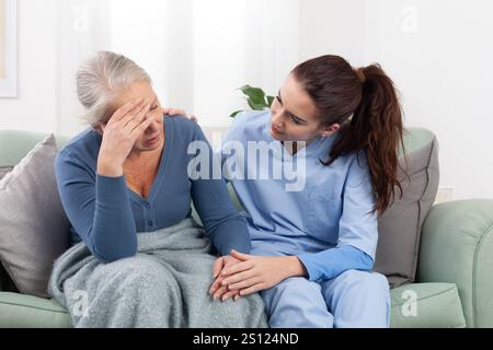 La cura di un giovane infermiere o medico conforta una paziente anziana che è turbata, stressata o preoccupata per un problema o un dolore. Assistenza domiciliare o in un me Foto Stock