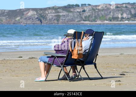 Coppia seduta su sedie da campeggio sulla spiaggia e sfidando il maltempo, Francia, Bretagna, Erquy Foto Stock