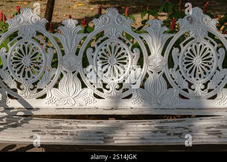 La luce naturale brilla colpendo la superficie dello schienale della panca da giardino in stile vittoriano in ghisa bianca. Dettaglio del banco in ghisa antica ornata in Foto Stock