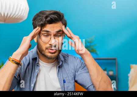 Uomo indiano malato che sfrega templi per curare problemi di mal di testa, soffre di tensione e emicrania, stress, dolore, pressione alta a casa. L'arabo indù è in camera sul divano Foto Stock
