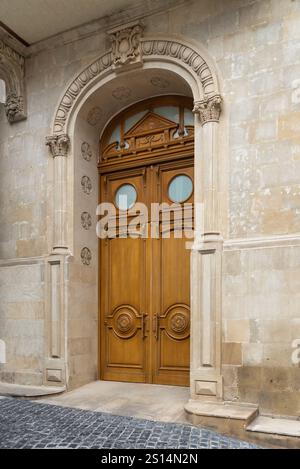 Un paio di porte in legno intagliate, caratterizzate da finestre circolari e modanature decorative, si trovano all'interno di un arco in pietra Foto Stock