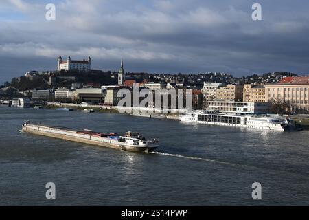 Bratislava, Slovacchia. 24 dicembre 2024. Una nave da carico naviga sul Danubio nella capitale Bratislava. La foto mostra la parte storica della città, incluso il castello di Bratislava. Nell'ambito del pacchetto di consolidamento del governo slovacco, a partire dal 1° gennaio 2025 l'aliquota di base dell'imposta sul valore aggiunto (IVA) aumenterà dal 20 al 23%, l'imposta sul reddito delle società aumenterà e in Slovacchia verrà introdotta una nuova imposta sulle transazioni finanziarie. (Immagine di credito: © Tomas Tkacik/SOPA Images via ZUMA Press Wire) SOLO PER USO EDITORIALE! Non per USO commerciale! Foto Stock