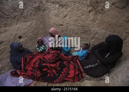 Lo sfollato palestinese Tayseer Obeid, 41 anni, originario della città di Gaza, scava un buco sotto il suolo nell'area di al-Zawaida della Striscia centrale di Gaza, lo sfollato palestinese Tayseer Obeid, 41 anni, originario della città di Gaza, scava un buco sotto il suolo nell'area di al-Zawaida della Striscia centrale di Gaza il 31 dicembre 2024. Con una carenza di tavole di legno e plastica per costruire una tenda adeguata per la sua famiglia, ricorre a questo metodo per fornire riparo. Il buco serve anche a proteggere i suoi figli e la sua famiglia dai bombardamenti israeliani casuali e a proteggerli dal freddo amaro. Da un lato del buco, Obeid Foto Stock