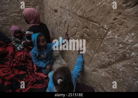 Lo sfollato palestinese Tayseer Obeid, 41 anni, originario della città di Gaza, scava un buco sotto il suolo nell'area di al-Zawaida della Striscia centrale di Gaza, lo sfollato palestinese Tayseer Obeid, 41 anni, originario della città di Gaza, scava un buco sotto il suolo nell'area di al-Zawaida della Striscia centrale di Gaza il 31 dicembre 2024. Con una carenza di tavole di legno e plastica per costruire una tenda adeguata per la sua famiglia, ricorre a questo metodo per fornire riparo. Il buco serve anche a proteggere i suoi figli e la sua famiglia dai bombardamenti israeliani casuali e a proteggerli dal freddo amaro. Da un lato del buco, Obeid Foto Stock