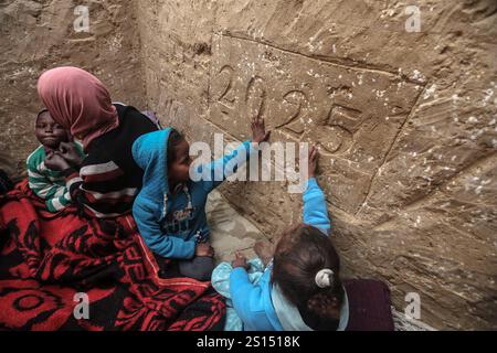 Lo sfollato palestinese Tayseer Obeid, 41 anni, originario della città di Gaza, scava un buco sotto il suolo nell'area di al-Zawaida della Striscia centrale di Gaza, lo sfollato palestinese Tayseer Obeid, 41 anni, originario della città di Gaza, scava un buco sotto il suolo nell'area di al-Zawaida della Striscia centrale di Gaza il 31 dicembre 2024. Con una carenza di tavole di legno e plastica per costruire una tenda adeguata per la sua famiglia, ricorre a questo metodo per fornire riparo. Il buco serve anche a proteggere i suoi figli e la sua famiglia dai bombardamenti israeliani casuali e a proteggerli dal freddo amaro. Da un lato del buco, Obeid Foto Stock