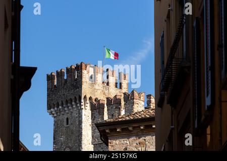 Sirmione, Italia - 21 settembre 2024: Torre del Castello Scaligero, con la bandiera italiana che sventola con grazia contro un cielo azzurro Foto Stock