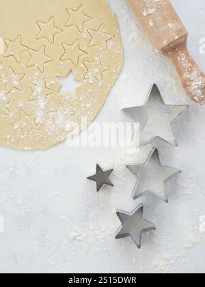 Cottura in forno a casa, impasto di pasta sfoglia con taglierine a stella di diverse dimensioni. Il mattarello di legno e la farina cosparse sul tavolo, visto dall'alto Foto Stock