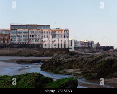 Spiaggia rocciosa con gli edifici storici della Medina alle spalle circondata da mura nella città di Essaouira, 31 dicembre 2024 Foto Stock