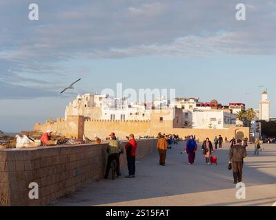 Turisti e gente del posto accanto alle mura della città con la storica Medina alle spalle e la costa rocciosa lasciata nella città di Essaouira, 31 dicembre 2024 Foto Stock