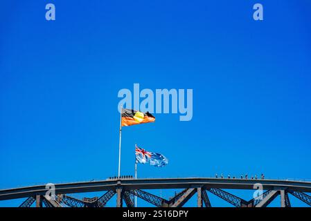 Persone che camminano sulla cima del Sydney Harbour Bridge (Bridge Climb) con la bandiera nazionale australiana e le bandiere aborigene indigene che sventolano Foto Stock