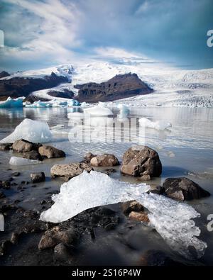 La maestosa cascata del ghiacciaio Fjallsjökull si estende lungo un aspro versante montano dagli altipiani, la sua distesa ghiacciata incontra le tranquille acque di Fjallsárlón gla Foto Stock