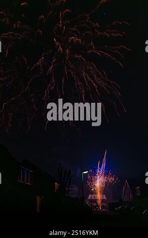 Incredibile spettacolo di fuochi d'artificio catturato durante le celebrazioni di Capodanno 2025, illuminando il cielo notturno su un quartiere residenziale Foto Stock