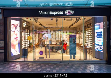 L'Optician Vision Express sulla strada principale della città merseyside di Liverpool con un cliente in un cappotto rosso che guarda fuori dalla porta della finestra Foto Stock