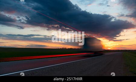 Sfocatura. Carrello in movimento su autostrada ad alta velocità. Nelle nuvole del cielo. Tramonto del sole all'orizzonte giallo-rosso brillante. Consegna del carico. Foto Stock
