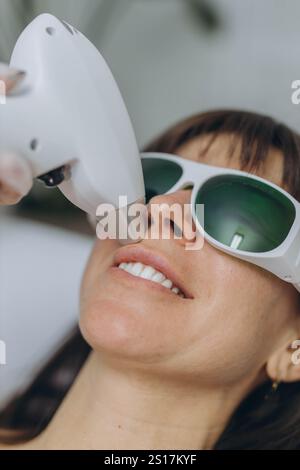 Cosmetologo professionista che esegue l'epilazione laser del viso su una donna che indossa occhiali protettivi. Foto di alta qualità Foto Stock