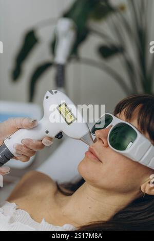 Cosmetologo professionista che esegue l'epilazione laser del viso su una donna che indossa occhiali protettivi. Foto di alta qualità Foto Stock