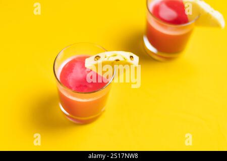 Succo di ananas in un primo piano di vetro vicino alla frutta tagliata a fette con spruzzi e liqid gocciolante per le vibrazioni estive. Sana bevanda biologica su sfondo arancione, c Foto Stock