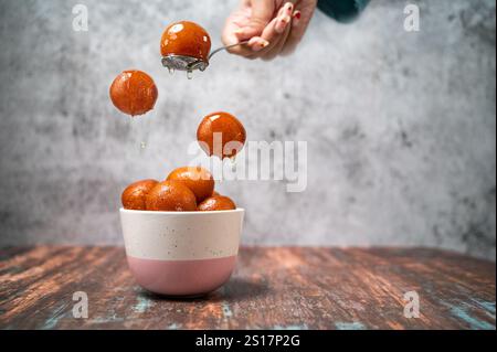 Una ragazza che serve Gulab Jamun in una ciotola con sciroppo dolce. Il Gulab Jamun è un dolce indiano a base di latte, preparato in occasione di feste o feste di nozze. Copia Foto Stock