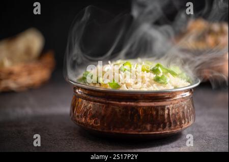 Riso bianco affumicato. Preparato e servito in una ciotola di ottone. Legno naturale sullo sfondo. Riso fritto in ciotola con piatto laterale su sfondo nero. copysp Foto Stock