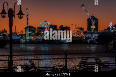 Un parco divertimenti vivace e colorato è splendidamente illuminato al crepuscolo da luci luminose che si riflettono sull'acqua Foto Stock