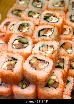 Pile di vivaci sushi roll presentano strati di pesce fresco, cetrioli croccanti e ripieno cremoso, il tutto avvolto in un tobiko arancione brillante. Un culi delizioso Foto Stock