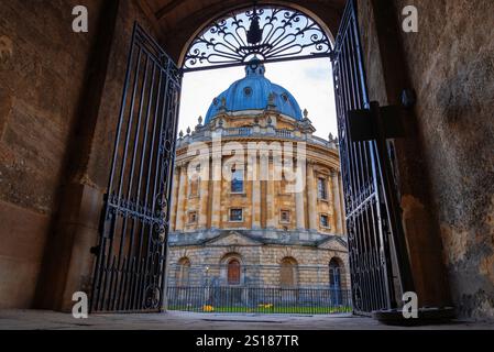 Oxford, Inghilterra: Vista incorniciata della Radcliffe camera attraverso i tassi di ferro ornati, che mostrano la storica architettura neoclassica e una prospettiva unica Foto Stock