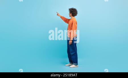 Uomo vestito con maglione arancione punta su sfondo blu studio Foto Stock