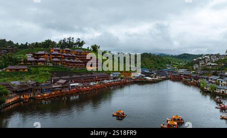 Vista aerea di un tranquillo villaggio di montagna annidato da un lago riflettente al crepuscolo, con luci calde che illuminano il paesaggio. Cieli nuvolosi e surrogati Foto Stock