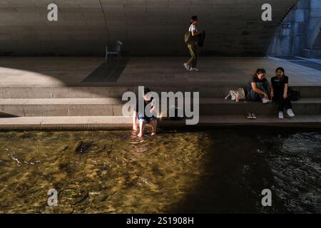 Le persone si rilassano e si immergono, immergono i piedi nell'acqua fresca accanto a un ponte di passaggio. Lungo il parco del fiume Cheonggyecheon a Seoul, Corea del Sud. Foto Stock