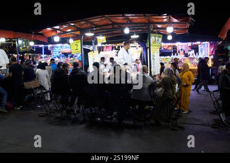 gente del posto seduta a mangiare lumache al cibo di strada in una delle bancarelle di cibo di sera in piazza jemaa el-fna a marrakech, marocco Foto Stock