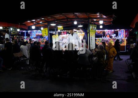 gente del posto seduta a mangiare lumache al cibo di strada in una delle bancarelle di cibo di sera in piazza jemaa el-fna a marrakech, marocco Foto Stock