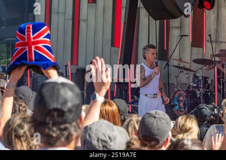 I fan mostrano la loro emozione mentre Robbie Williams sale sul palco in un concerto gratuito all'aperto, elettrizzante migliaia di persone a Melbourne, Australia. Robbie Williams, Rock Star, ha affascinato 8.000 fan alla Federation Square di Melbourne, riempiendo il locale fino alla sua massima capacità per un concerto gratuito che celebra il suo film Better Man. La soleggiata esibizione pomeridiana ha visto la folla cantare, ballare e applaudire mentre Robbie mostrava i suoi successi iconici. I fan hanno portato cartelli e sorrisi, creando un'atmosfera vivace e gioiosa. Questo evento indimenticabile ha sottolineato il legame di Robbie con il suo pubblico e la passione per Melbourne Foto Stock