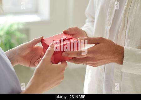 Persone che tengono in mano una confezione regalo rossa, marito che sorprende moglie con un regalo per San Valentino o anniversario Foto Stock