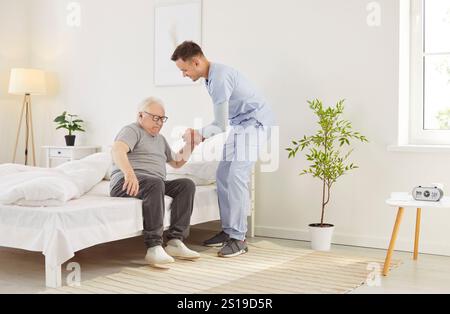 Medico o infermiere che assiste il paziente anziano fuori dal letto al mattino presso la casa di cura Foto Stock