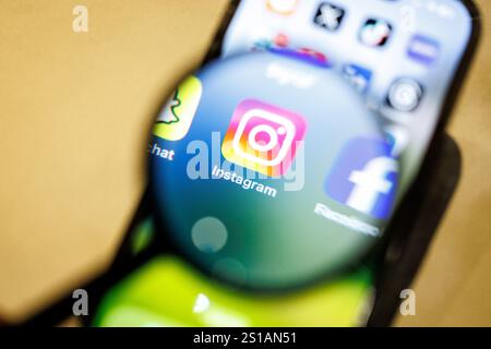 29 dicembre 2024, bassa Sassonia, Norden: Il logo dell'app Instagram può essere visto attraverso una lente di ingrandimento sul display di uno smartphone il 29 dicembre 2024. Instagram è un social network che si concentra sulla condivisione di video e foto ed è gestito da Meta Platforms. Foto: Matthias Balk/dpa Foto Stock