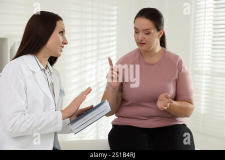 Nutrizionista con notebook che fornisce consigli alle donne in sovrappeso in ospedale Foto Stock