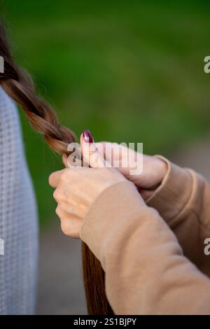 Vista delle mani femminili che tessono una treccia da lunghi capelli femminili Foto Stock