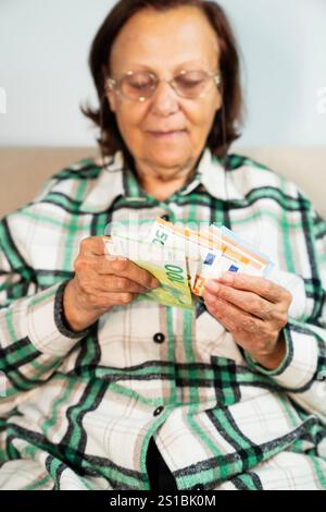 Primo piano delle mani di una donna anziana che tiene in mano una pila di banconote in euro Foto Stock