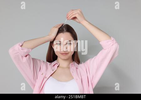 Problema di perdita dei capelli. Ragazza che applica il siero sulla linea di capelli su sfondo grigio Foto Stock