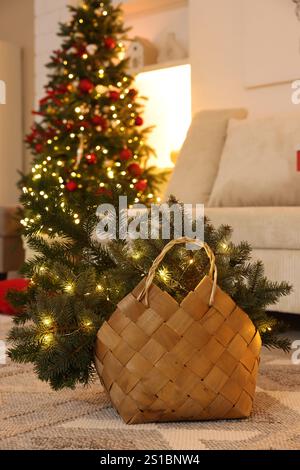 Cestino in vimini con rami di abeti e luci natalizie sul pavimento all'interno Foto Stock