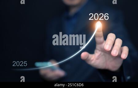 Felice anno nuovo. Un uomo d'affari, con il suo smartphone, disegna una linea in aumento, dal 2025 al 2026, che rappresenta la crescita mirata, il successo e il successo Foto Stock