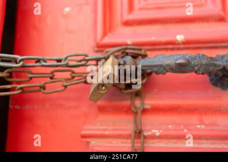 Primo piano di catene metalliche e serrature nelle maniglie su porte rosse vintage chiuse. Foto full frame di vibrante entrata in legno all'aperto. Foto Stock