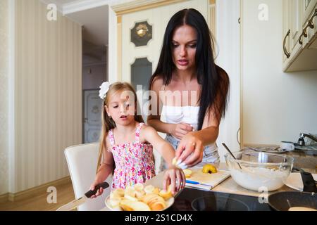 Mamma e figlia preparano l'insalata di frutta insieme in una cucina moderna durante il pomeriggio Foto Stock