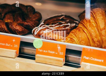 Delizioso assortimento di prodotti da forno presentati su uno scaffale da forno, con opzioni vegane a prezzi etichettati. Foto Stock