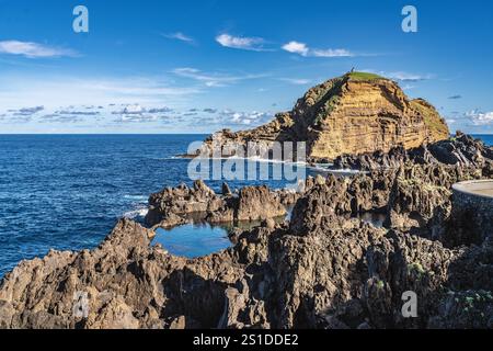 Scopri la tranquillità di questo aspro paesaggio costiero con una piscina naturale e viste panoramiche sull'oceano, circondato da impressionanti formazioni rocciose Foto Stock