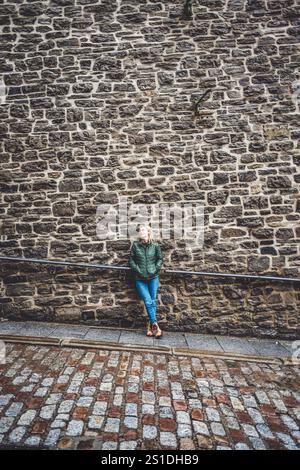 Bella giovane donna bionda si appoggia contro il muro di pietra in Quebec Foto Stock