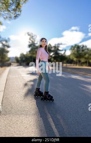 Una donna sportiva ama pattinare mentre ascolta musica con le cuffie in un parco soleggiato Foto Stock