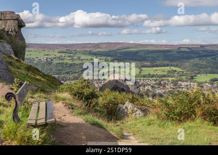 Un posto a sedere in legno accanto alle rocce di mucca e vitello su Ilkley Moor con vedute a lunga distanza sulla Wharfedale Valley. Foto Stock